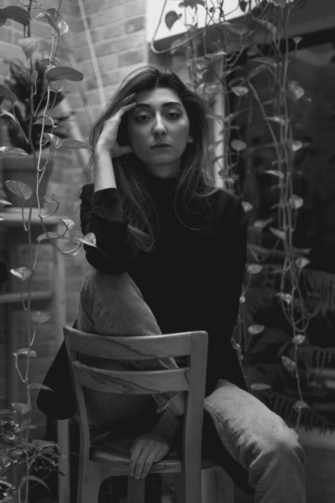 Black-and-white portrait of Mubie seated among hanging plants