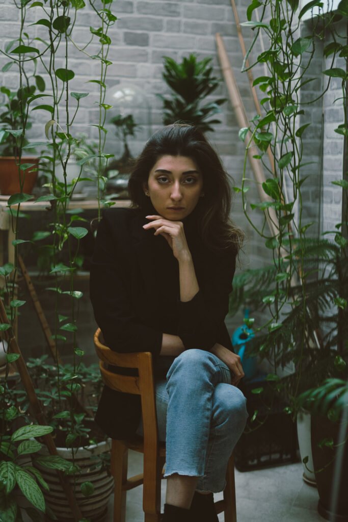 Mubie seated on a wooden chair surrounded by green plants