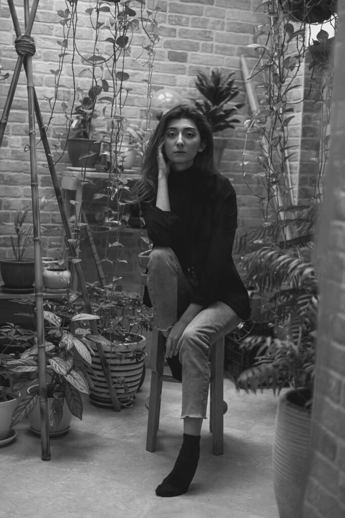 Black-and-white full-length portrait of Mubie seated among plants
