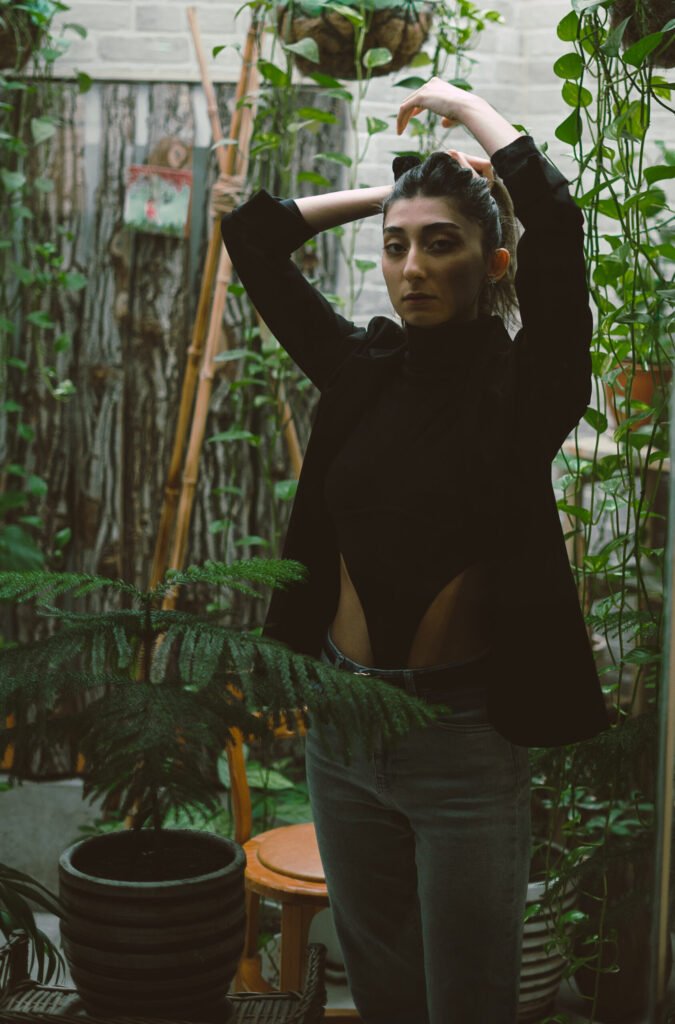 Mubie standing with her arms raised in a lush interior