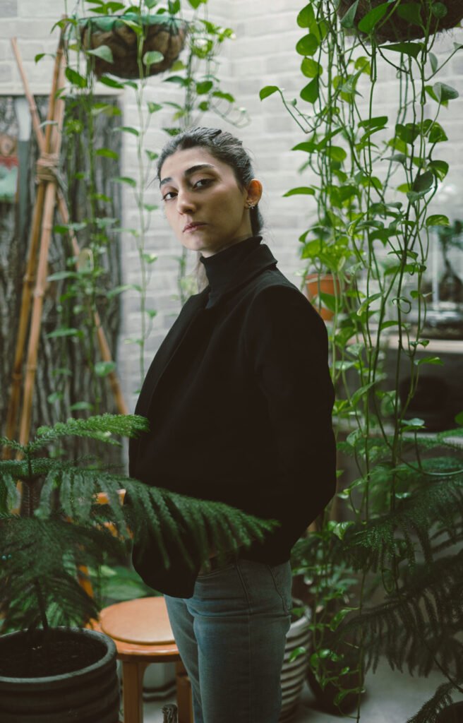 Profile portrait of Mubie standing beside hanging plants