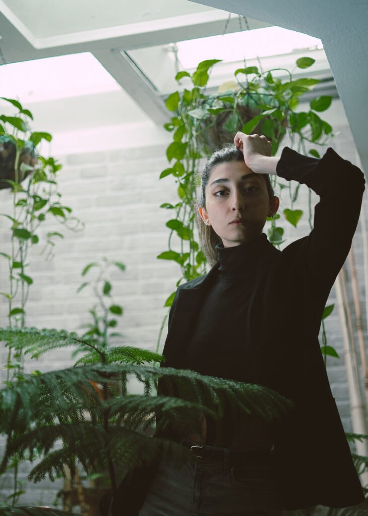 Low-angle portrait of Mubie beneath a skylight and hanging plants