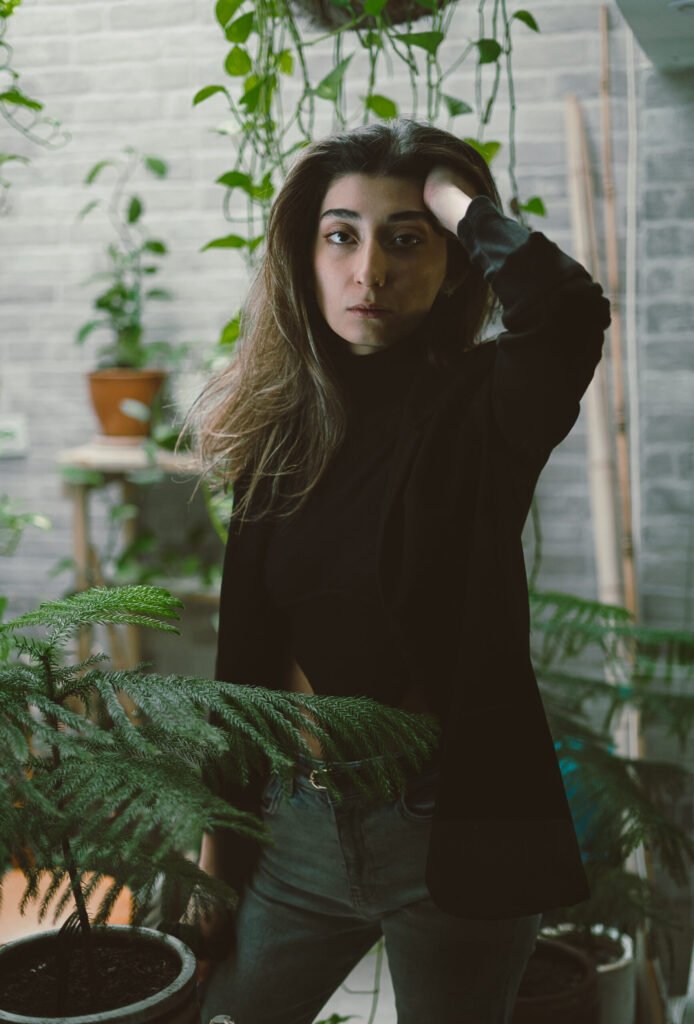 Editorial portrait of Mubie standing behind a potted evergreen