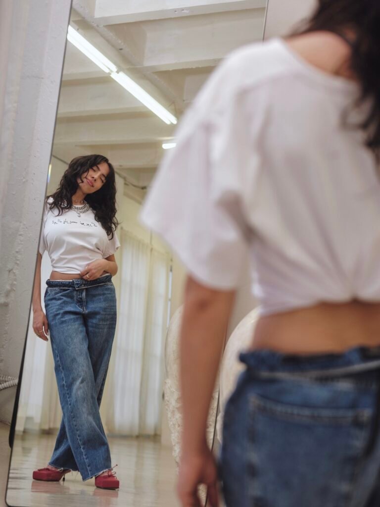 Neena Roe reflected in a studio mirror wearing a white T-shirt and jeans