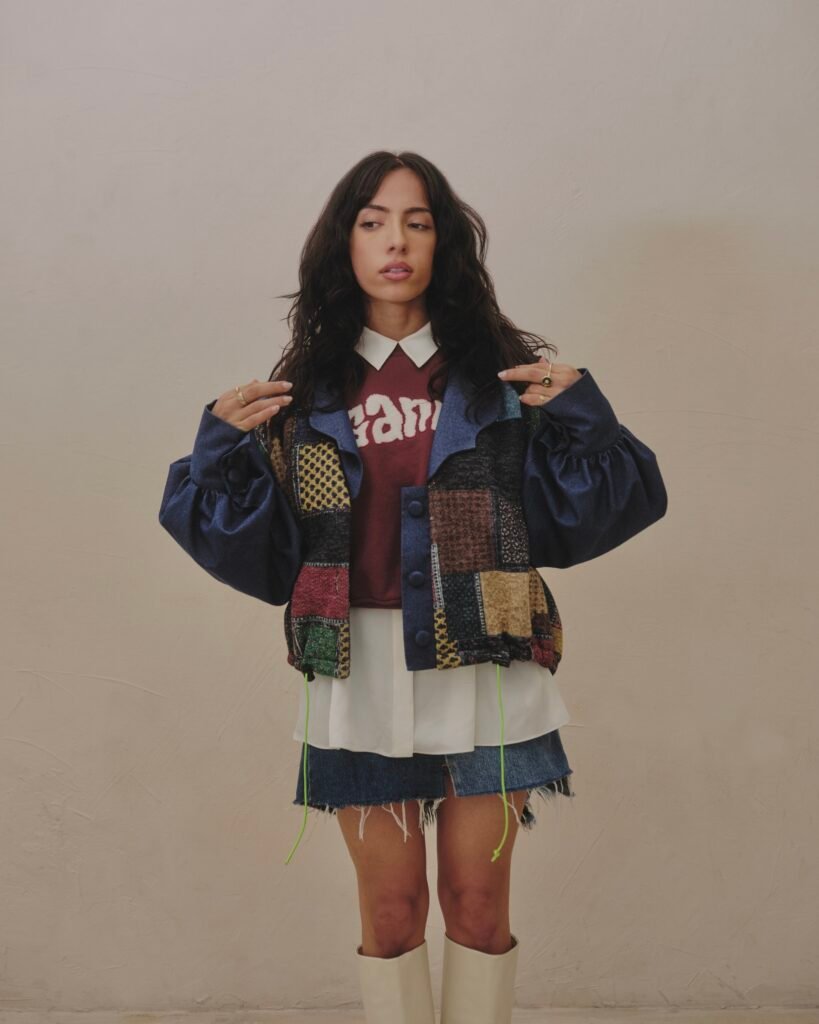 Full-length portrait of Neena Roe wearing a patchwork jacket and cream boots