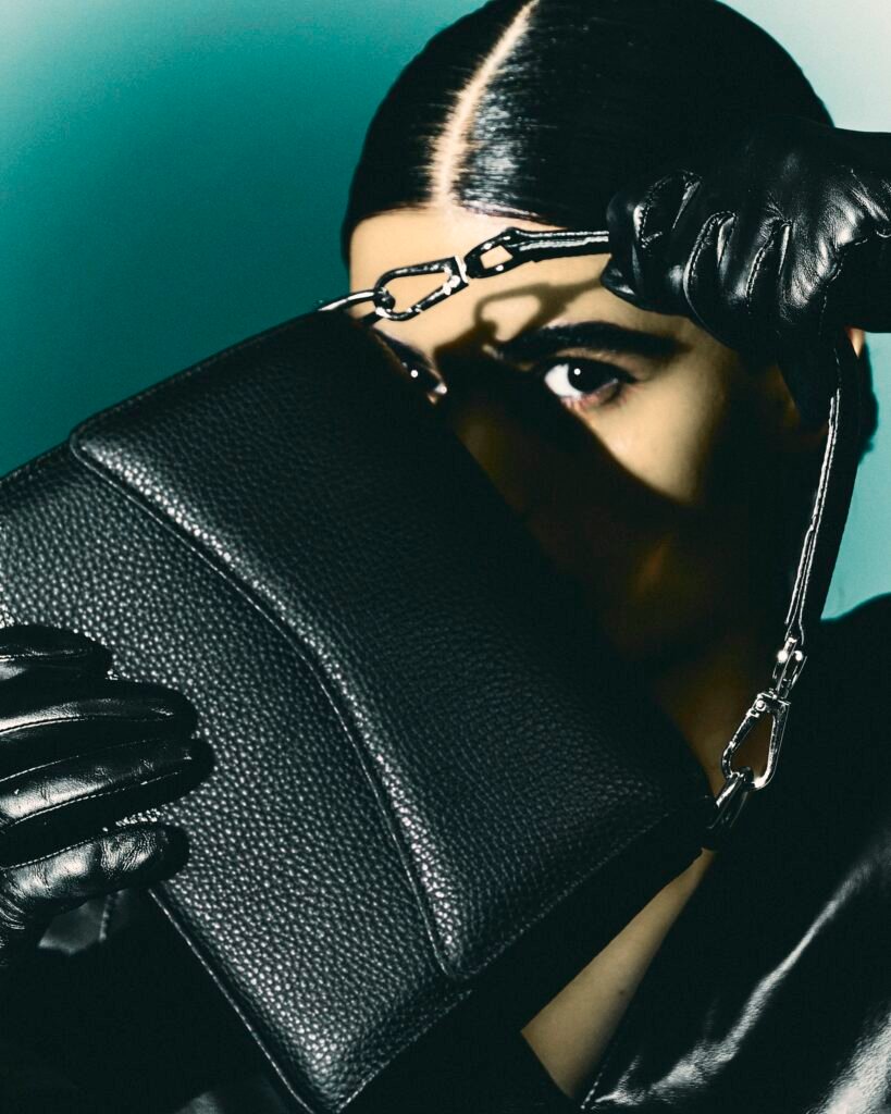 Close-up portrait framed by a black leather bag and gloves