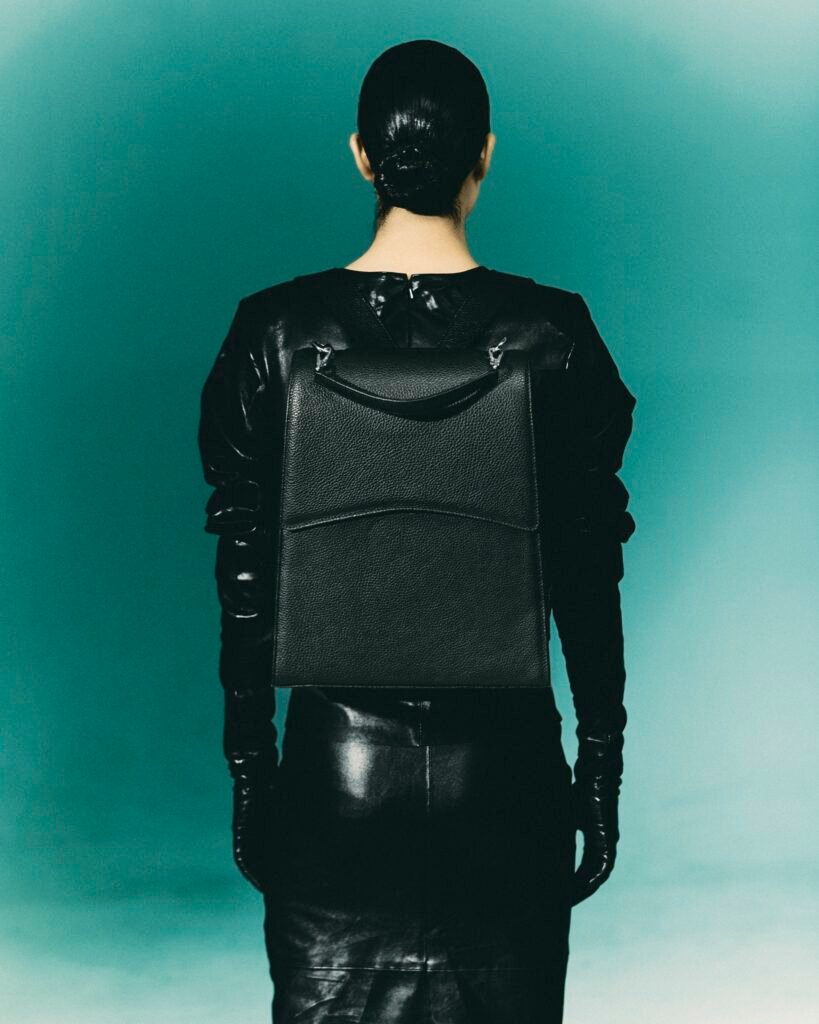 Model wearing a large black leather work bag as a backpack