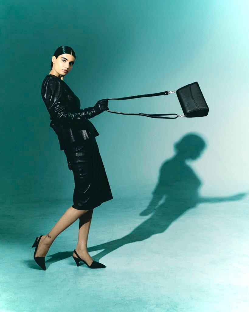 Model holding a small black leather bag by its long strap