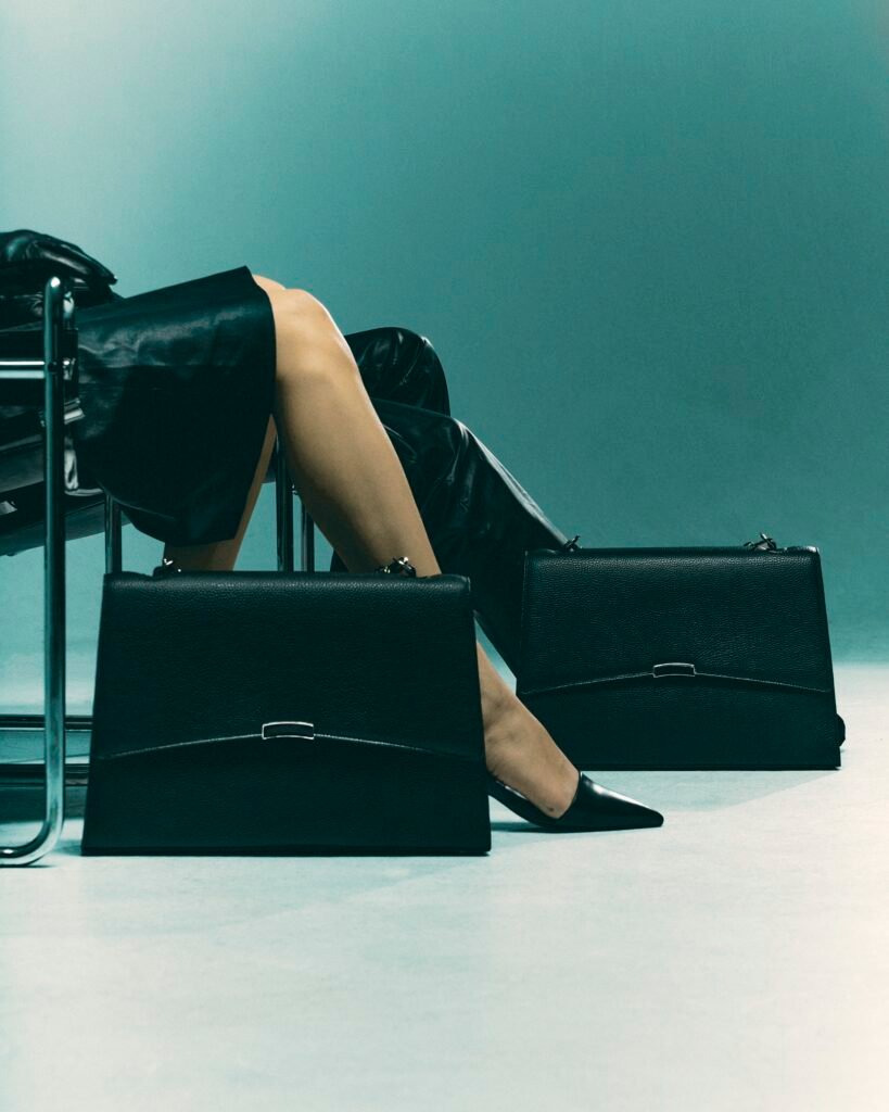 Two black leather work bags beside a seated model