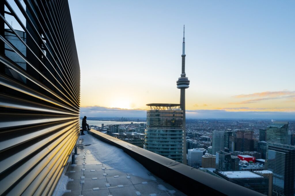 Urban explorer on a Toronto rooftop facing the CN Tower at sunset