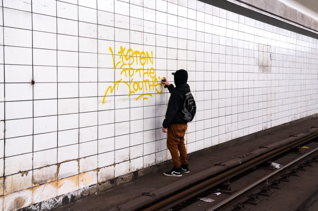 Graffiti artist painting Listen to the Youth on a tiled subway tunnel wall