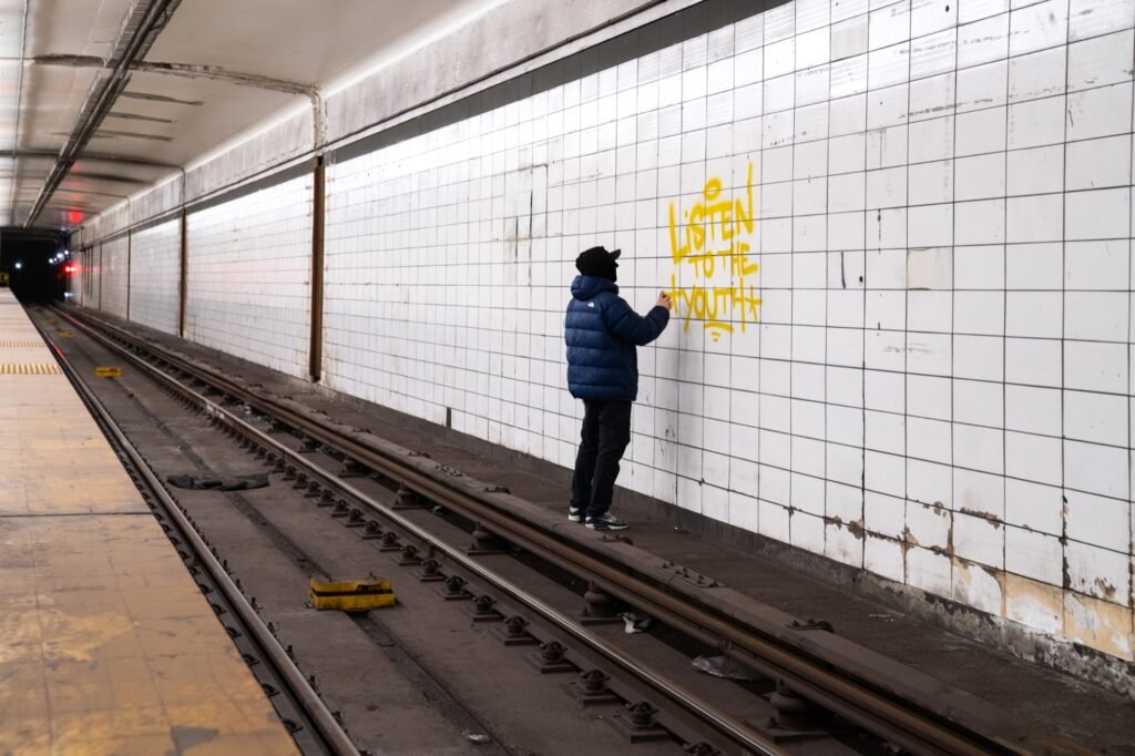 Graffiti artist painting a tiled wall beside subway tracks