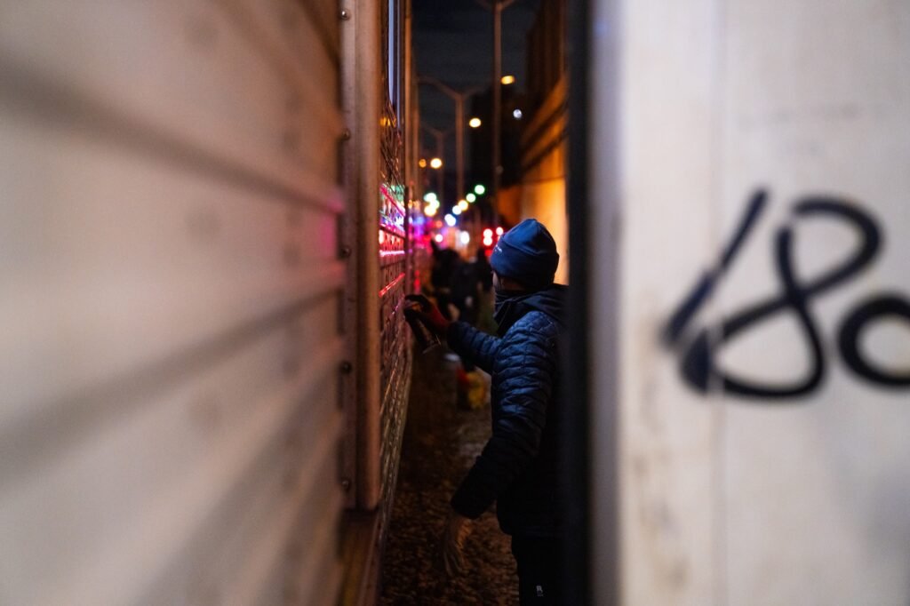 Graffiti artist painting a train between two rail cars at night