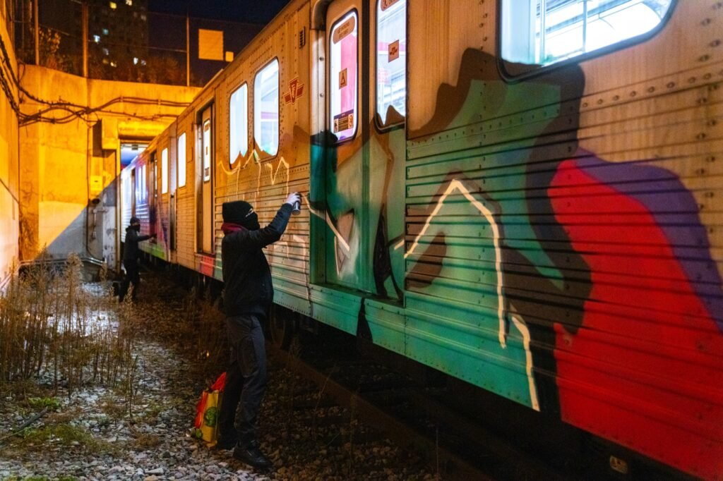 Two graffiti artists painting the side of a train at night