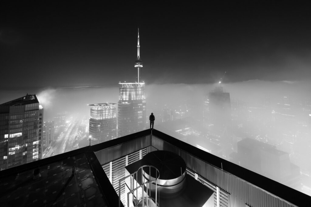 Urban explorer standing above a fog-covered Toronto skyline at night