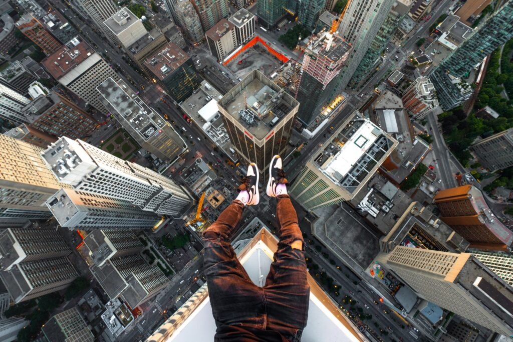 Urban explorer's legs extending over the edge of a skyscraper above city streets