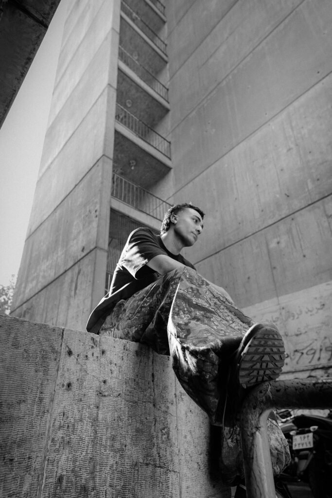 A black and white portrait of Emad siting on a ledge outside Ekbatan complex in Tehran.